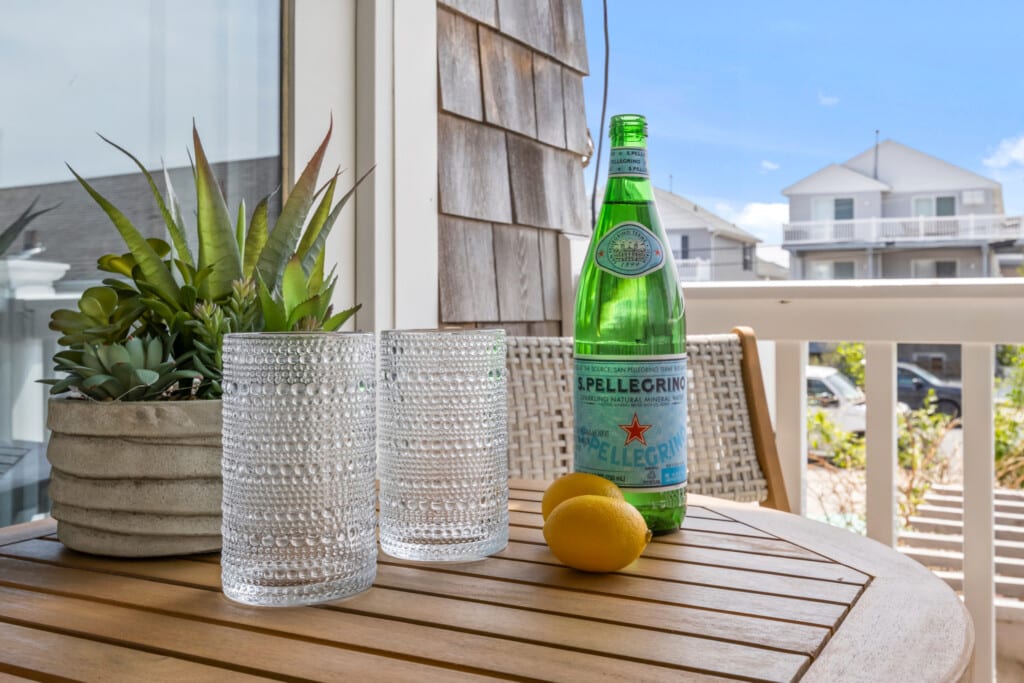 Sunny balcony table with a plant, two empty glasses, two lemons, and a bottle of water in bright natural light.