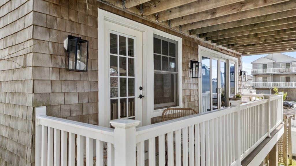 Sunny balcony with white walls, white doors and windows, two tables with chairs, and string lights creating a warm, inviting atmosphere.
