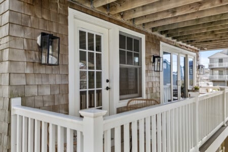 Sunny balcony with white walls, white doors and windows, two tables with chairs, and string lights creating a warm, inviting atmosphere.