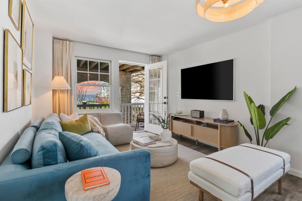 Living room with sunset view, blue bed and sofa, wall-mounted TV, and a beautiful green plant in the corner.