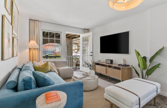 Living room with sunset view, blue bed and sofa, wall-mounted TV, and a beautiful green plant in the corner.