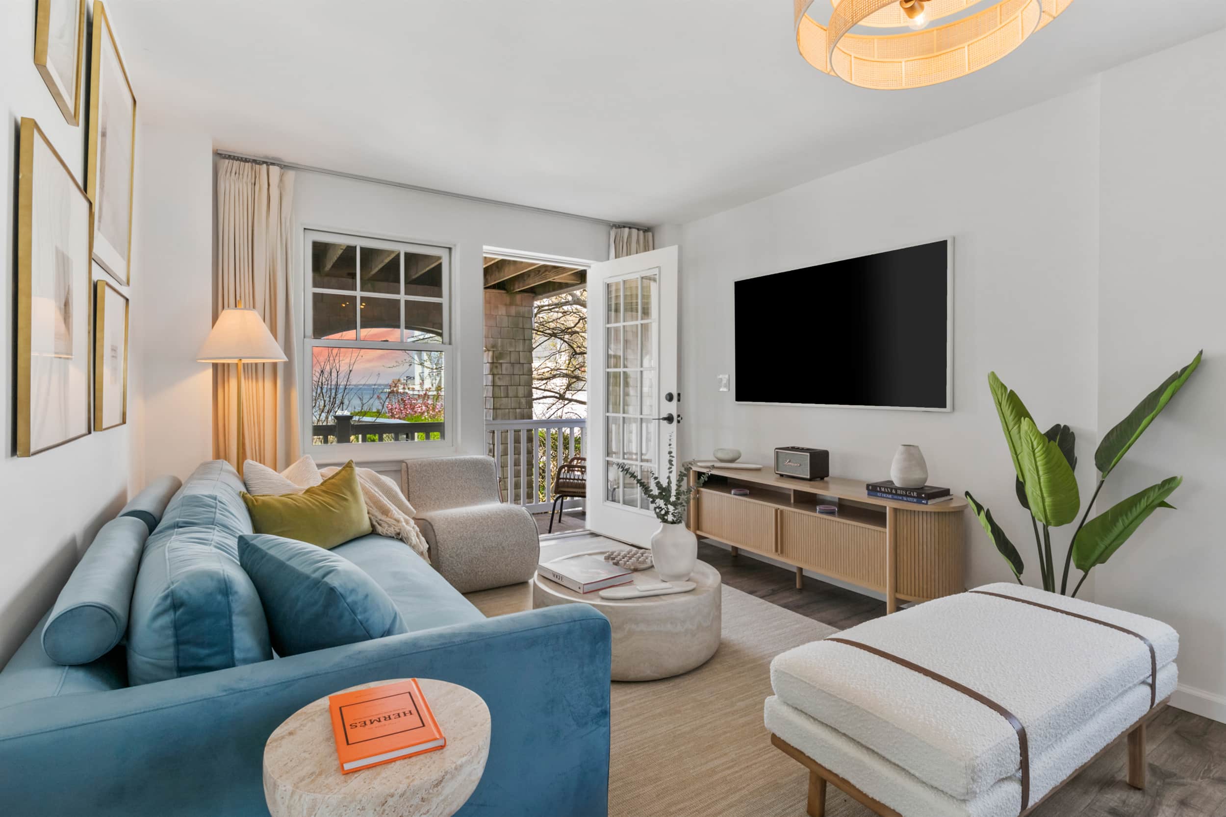 Living room with sunset view, blue bed and sofa, wall-mounted TV, and a beautiful green plant in the corner.