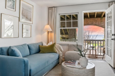 Living room with a sunset view, comfy blue couch, white sofa, and a vase with a book on the table.