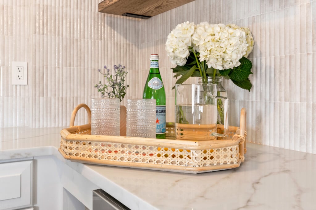 Tray holding two glasses and water bottle, with a vase of white flowers behind it.