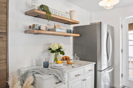 White table with water, muffins, lemons, white flowers, grey fridge, and a decorative “Beach House” sign.